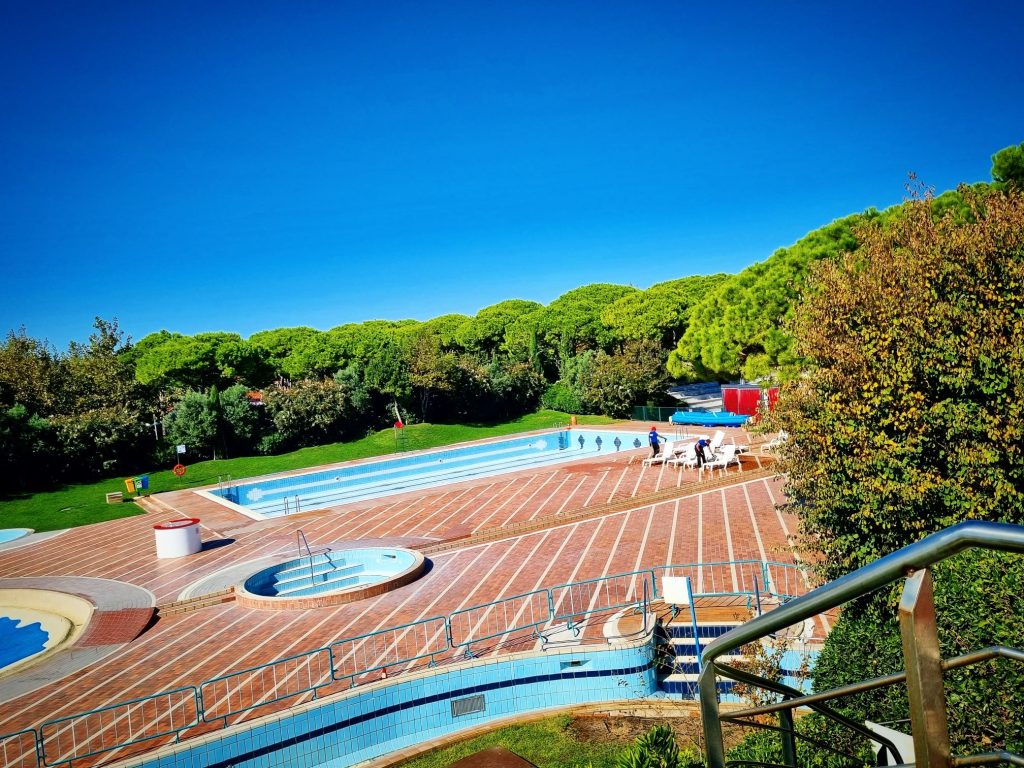 Weitwinkelaufnahme des Poolbereichs im Aquapark Mare des Union Lido in Cavallino, Italien, am Ende der Sommersaison. Alle Schwimmbecken sind vollständig entleert und die Poolbereiche mit Absperrungen gesichert. Zu sehen sind die leeren Becken, Sonnenterrassen, Liegen und Treppen rund um die Anlage.