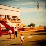 Farbfotografie der Piazza Lido im Union Lido in Cavallino, Italien, aus dem Jahr 1987. Zu sehen sind das damalige Gebäude mit markanter roter Außentreppe, eine überdachte Terrasse, Sonnenschirme, Union-Lido-Flaggen und Besucher auf dem Vorplatz.