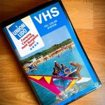 HS-Videokassette von Union Lido mit einem Titelbild, das Wassersport auf dem Meer und den Strand mit Sonnenschirmen zeigt. Das Cover trägt das Union-Lido-Logo sowie die Aufschrift „Camping, Caravanning, Hotel, Bungalow, Sport“ und „VHS PAL Color System“.