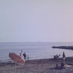 Historische Aufnahme des Strandes von Union Lido in Cavallino aus dem Jahr 1969 mit Badegästen, Sonnenschirmen, dem Meer und einem steinernen Wellenbrecher.