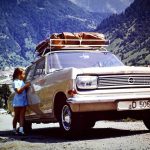 Historische Aufnahme der Anreise über den Brenner im Jahr 1966. Ein Opel Rekord mit Gepäck auf dem Dach steht vor einer alpinen Berglandschaft, während ein Mädchen neben dem Fahrzeug steht. Die Aufnahme zeigt die typische Urlaubsreise mit dem Auto über die Alpen in Richtung Italien.