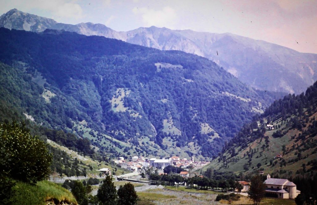 Historische Aufnahme der Anreise über den Brenner im Jahr 1966 mit Blick auf eine alpine Berglandschaft und ein Bergdorf im Tal. Die Aufnahme entstand während der Fahrt in Richtung Italien und zeigt die Landschaft entlang der Brennerroute.